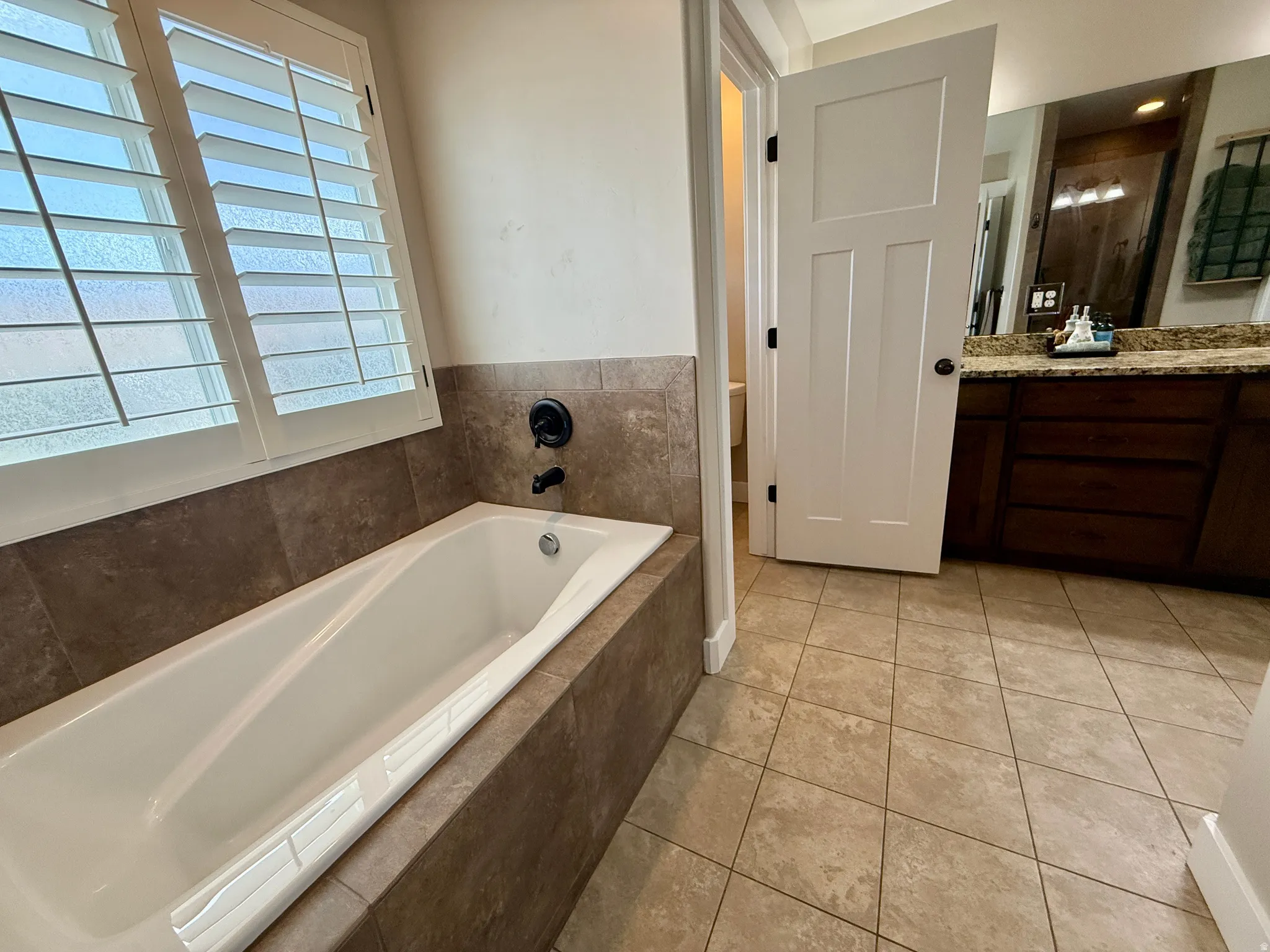 Soaking tub with surrounding tile, white plantation shutters, and matte black fixtures
