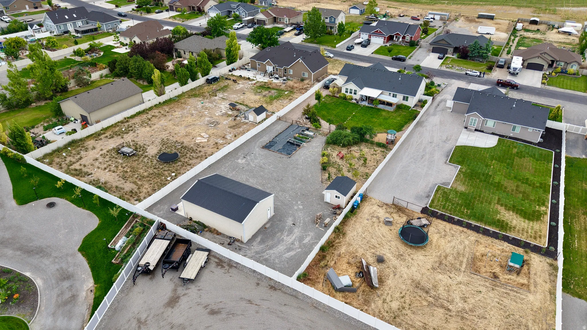 Expansive lot featuring a large detached garage with a black metal roof, gravel surfacing, and white perimeter fencing