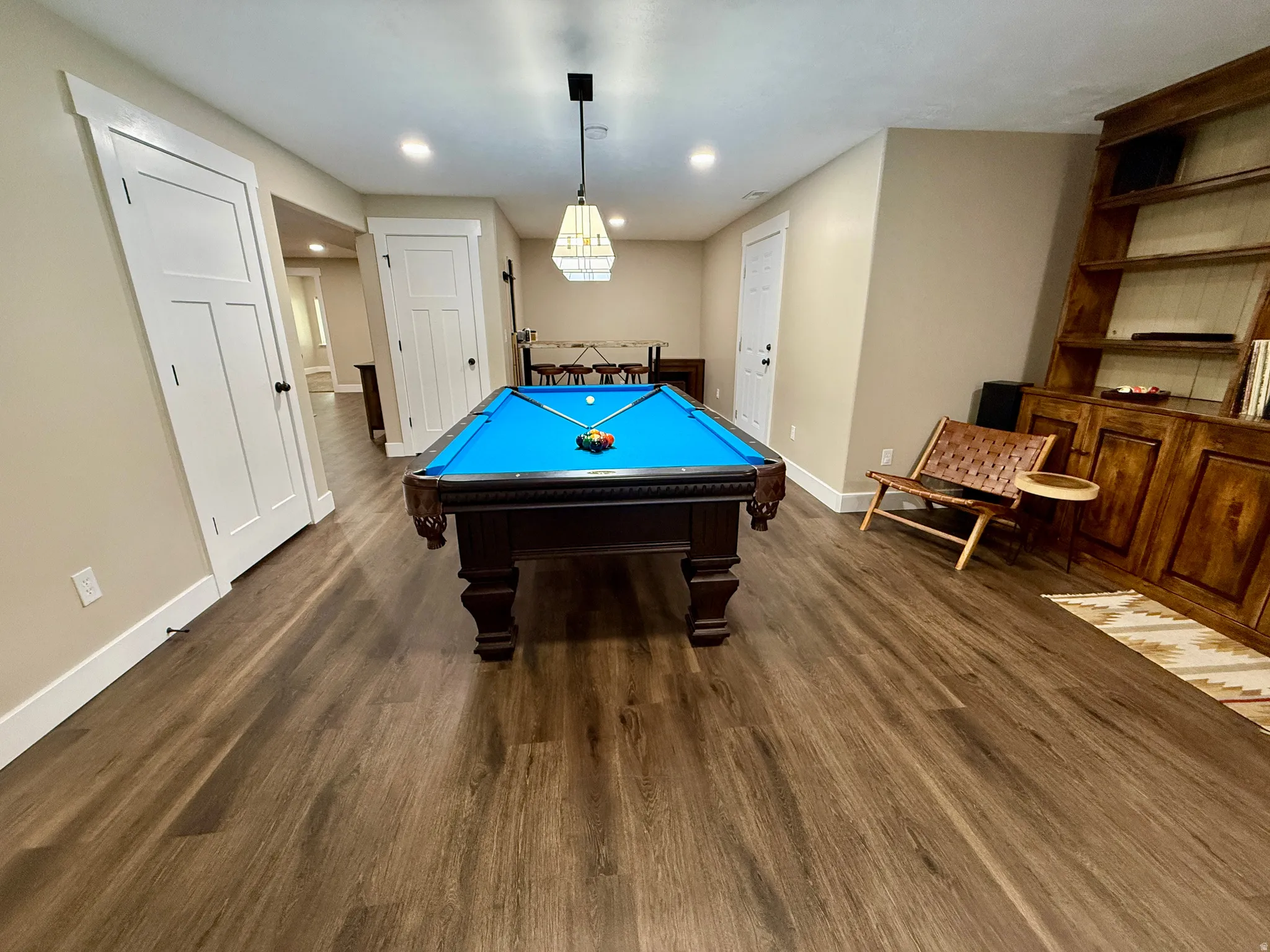 Spacious recreation room featuring wood-finish flooring, recessed lighting, and a prominent built-in wood shelving unit