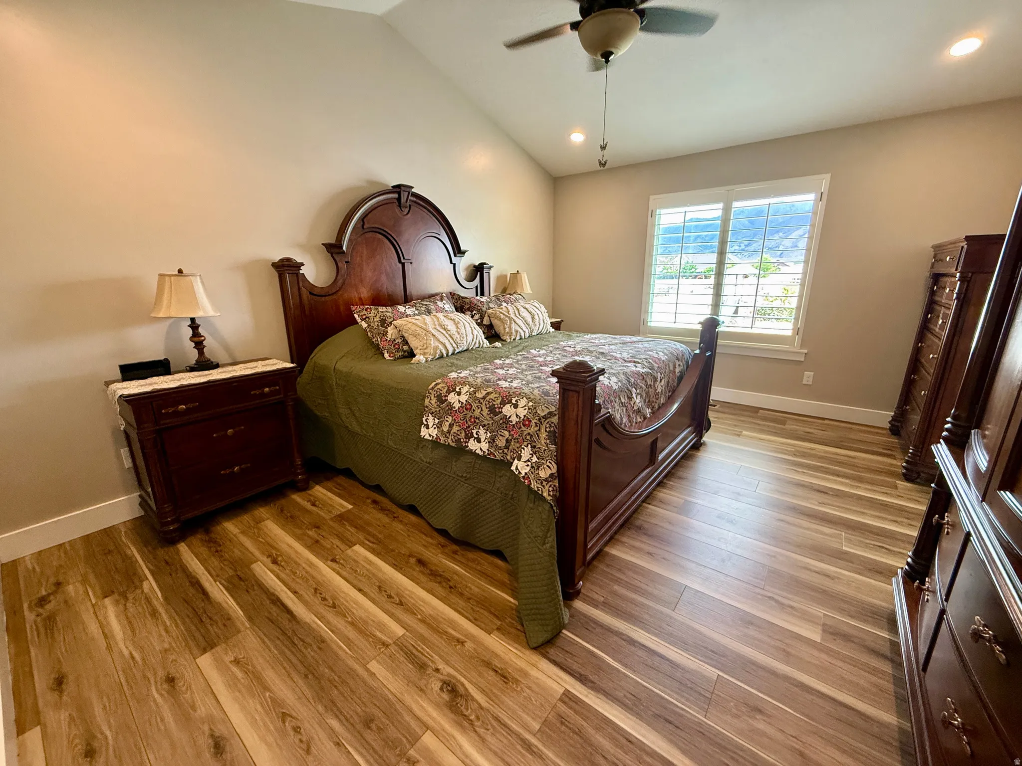 Spacious bedroom featuring vaulted ceilings, wood-finish flooring, a ceiling fan with integrated lighting, and plantation shutters