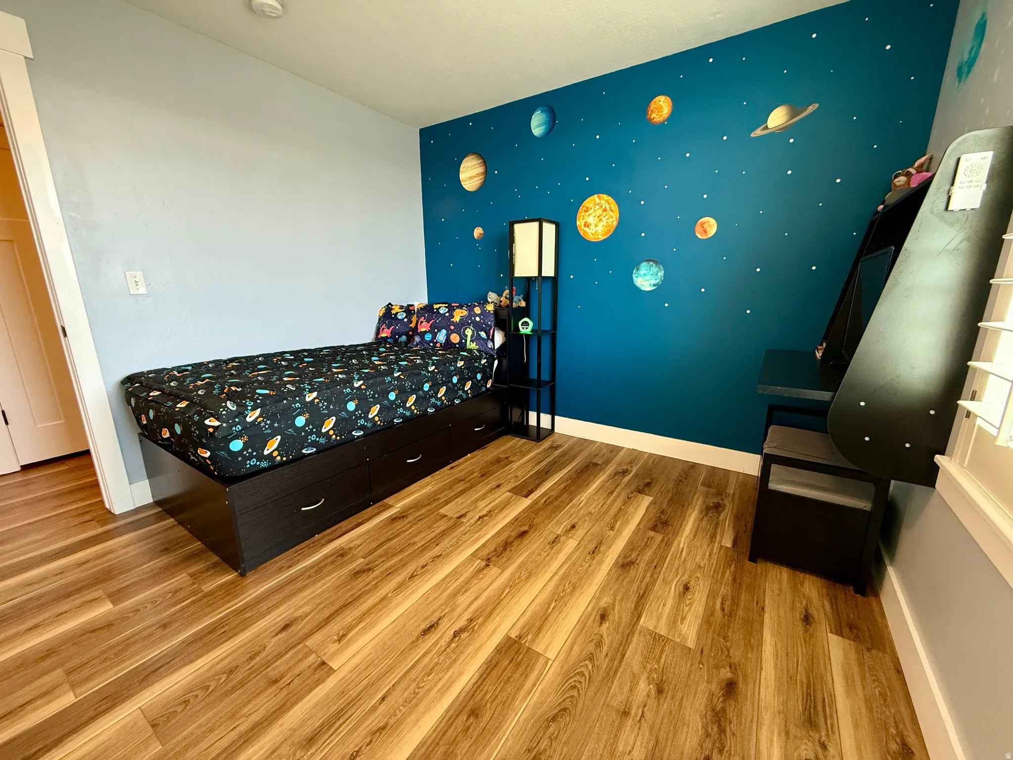 Spacious room featuring wood-finish flooring, a vibrant accent wall, and white baseboards