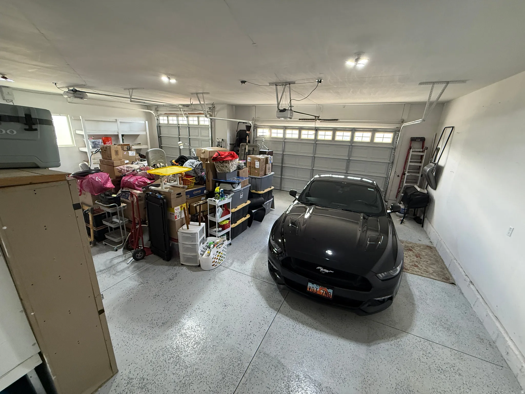 Three-car garage featuring a speckled epoxy floor coating, multiple overhead lighting fixtures, and two garage doors with window inserts