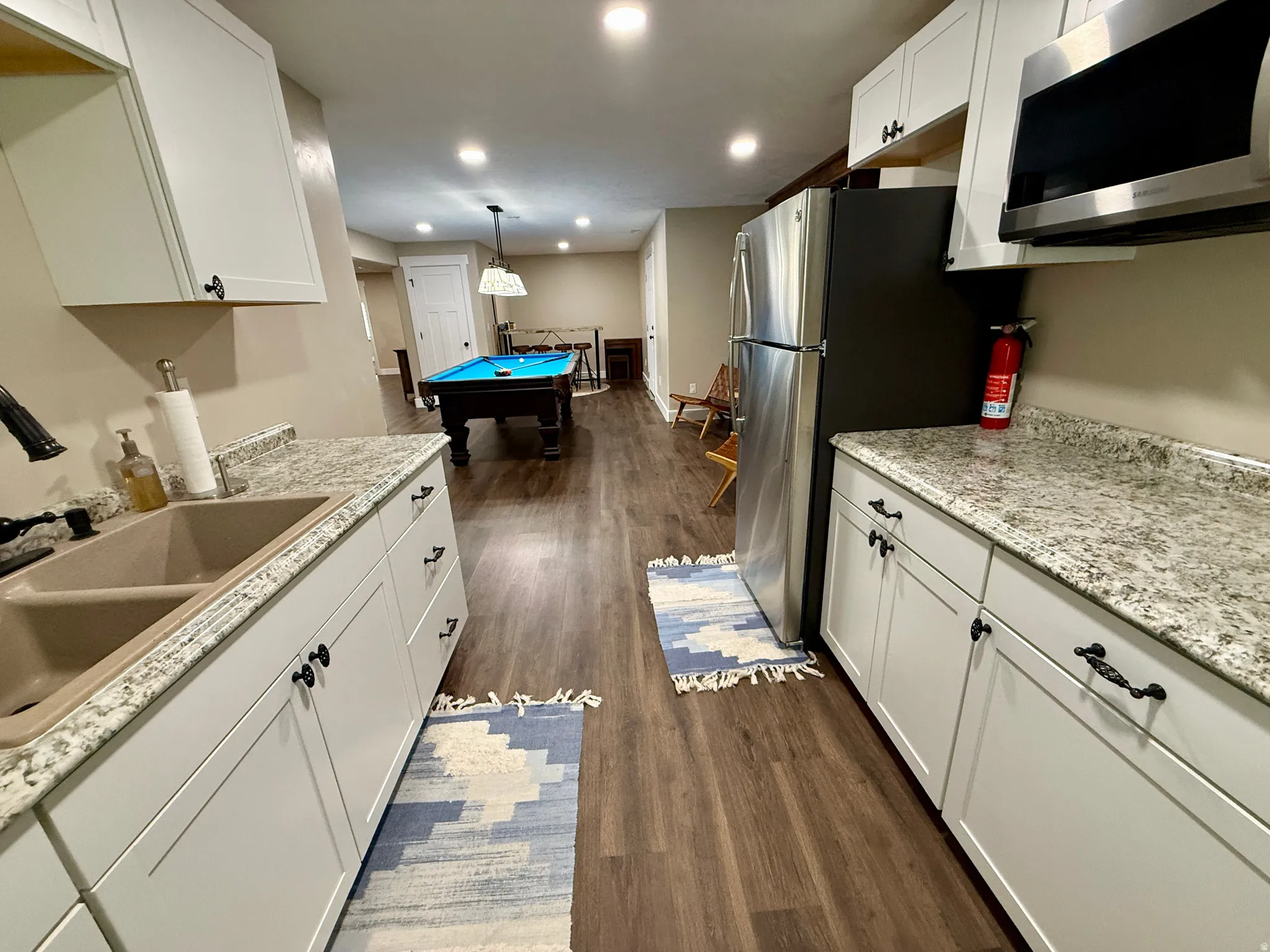 Kitchenette featuring white cabinetry, light-toned countertops, a double basin sink, and stainless steel appliances, all complemented by wood-finish flooring