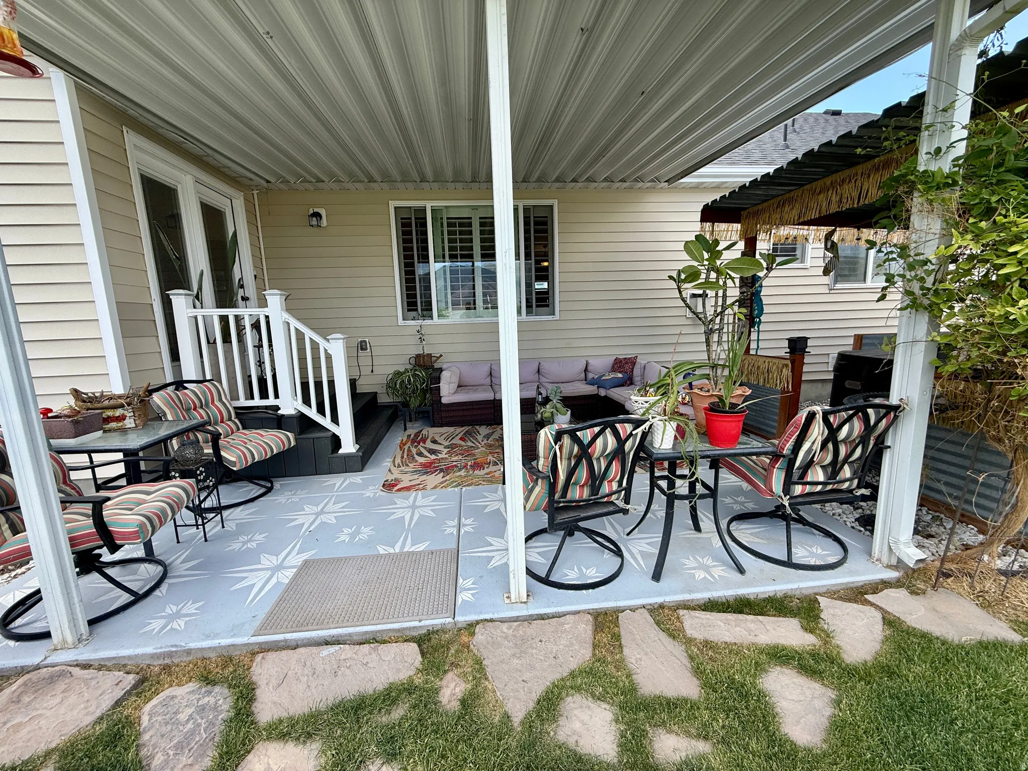 Covered patio with a patterned concrete surface, featuring direct access via a double glass door, white railing, and a stepped entry