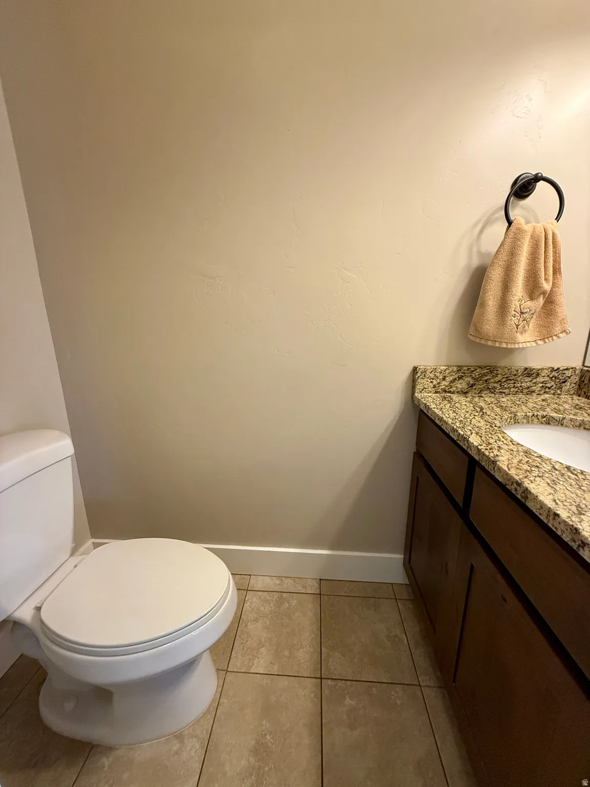 Bathroom featuring a white toilet, tiled flooring, a dark wood-finish vanity with a granite countertop, and an undermount sink