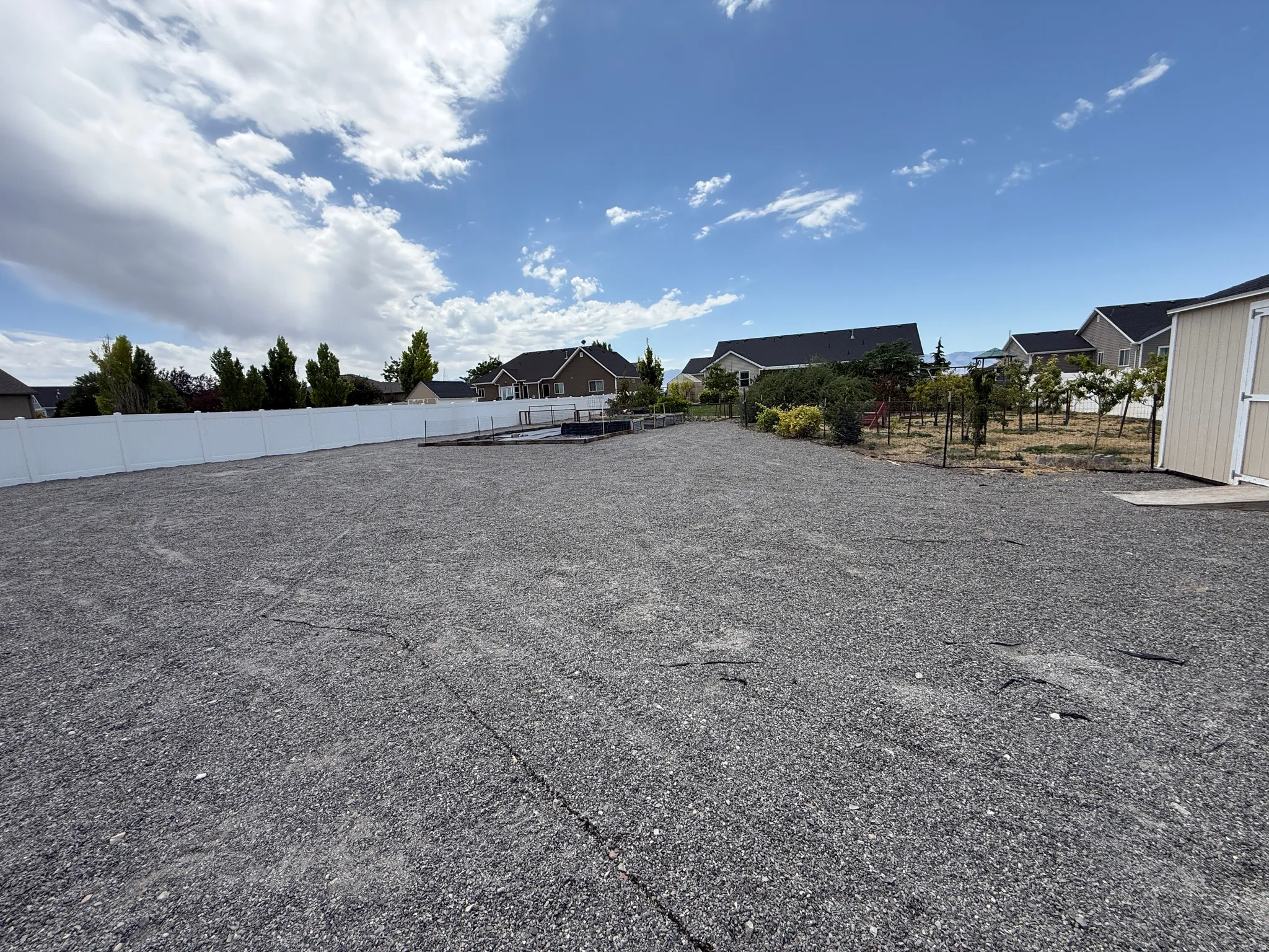 Expansive gravel yard featuring a white privacy fence, an unpaved surface, and a detached storage shed