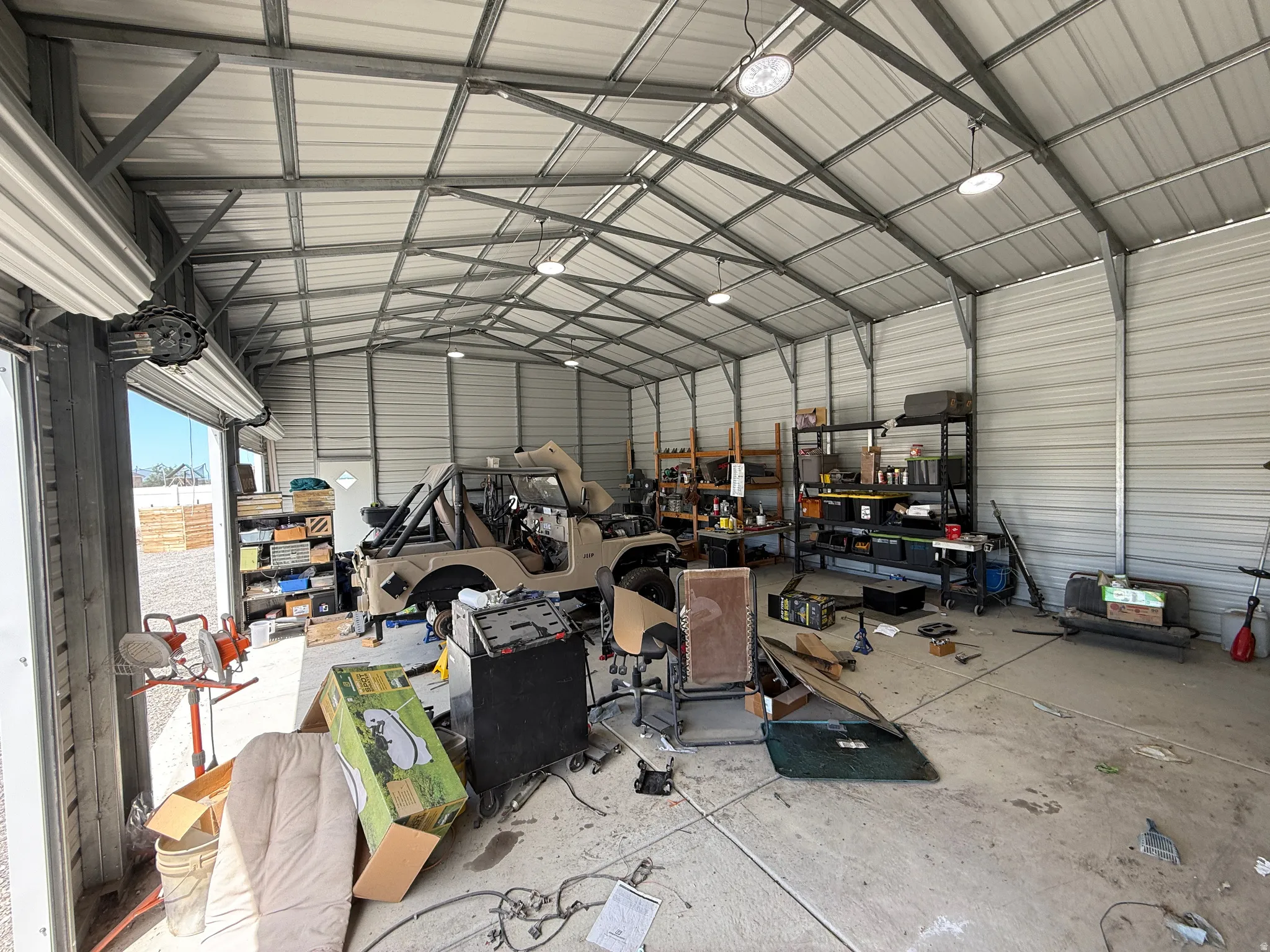 Spacious metal-frame building featuring a concrete slab floor, corrugated metal walls and ceiling, multiple overhead light fixtures, and a large roll-up door