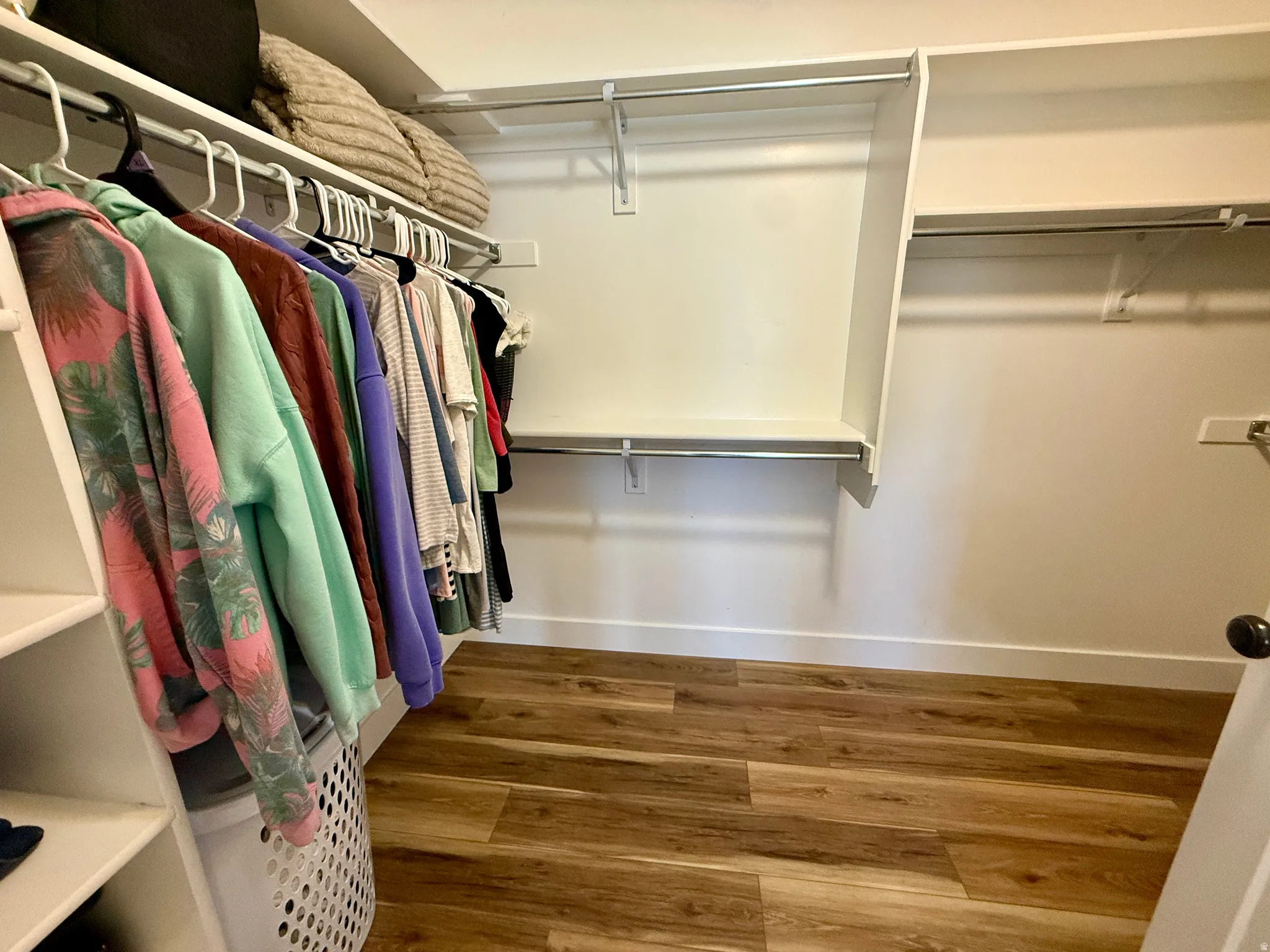 Walk-in closet featuring wood-finish flooring, white baseboards, and built-in shelving with hanging rods