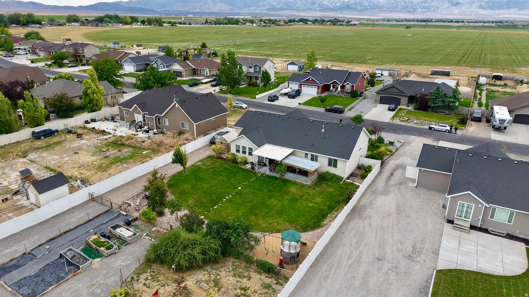 Expansive residential property featuring a large backyard, paved driveway, mature landscaping, white privacy fencing, and a covered patio