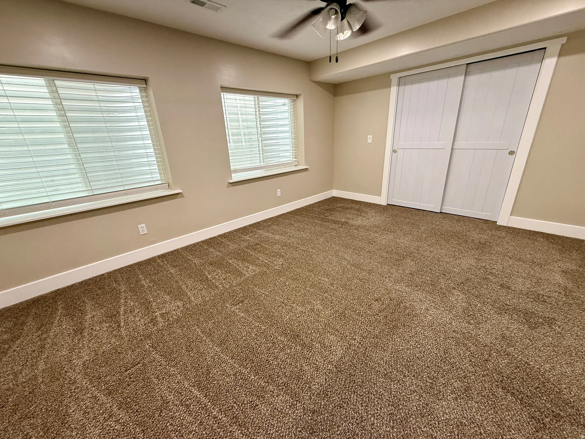 Bedroom featuring two windows with blinds, plush brown carpeting, a ceiling fan, and white sliding closet doors