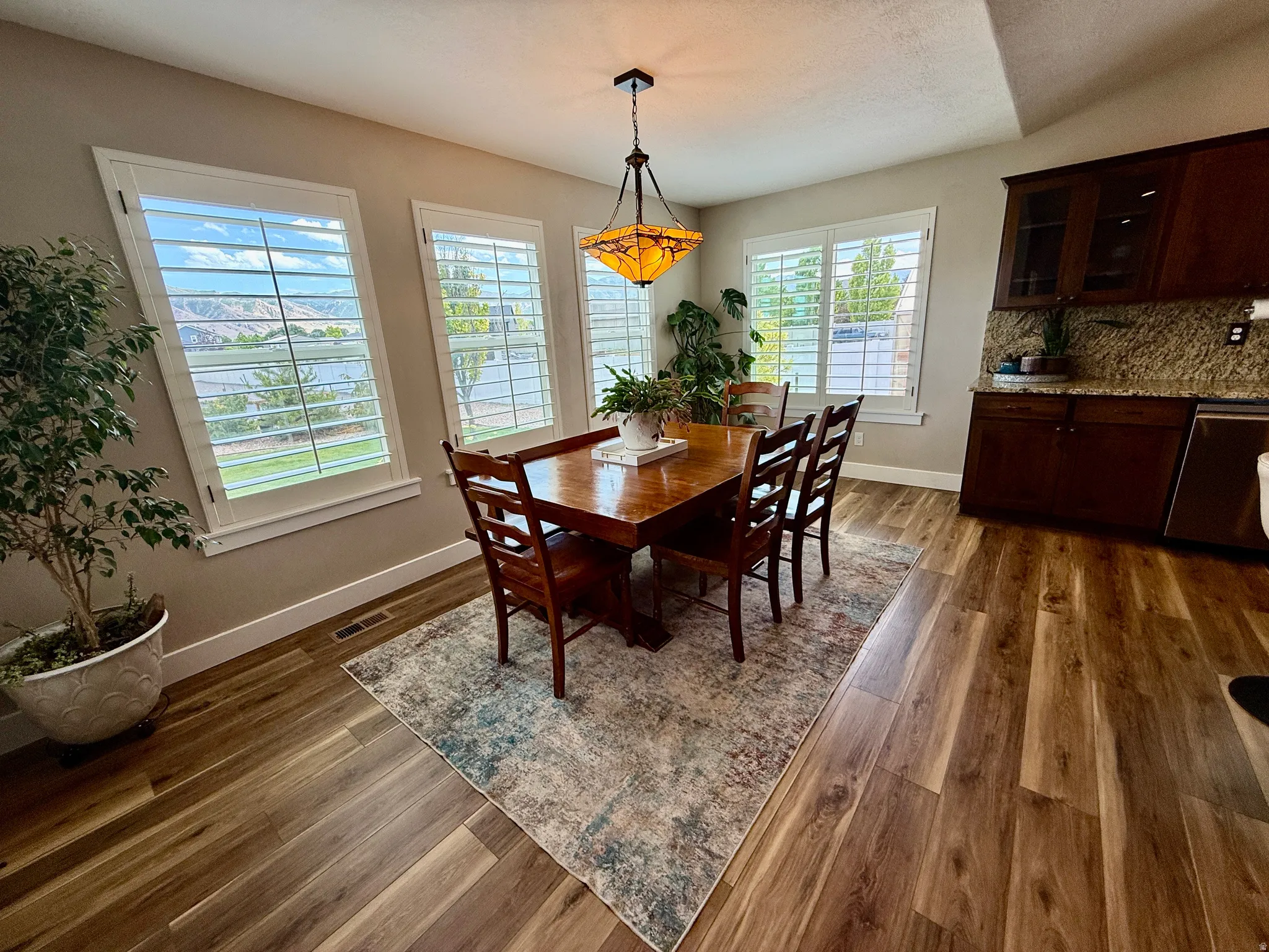 Dining area featuring wood-finish flooring, multiple windows with white plantation shutters, and a decorative pendant light fixture