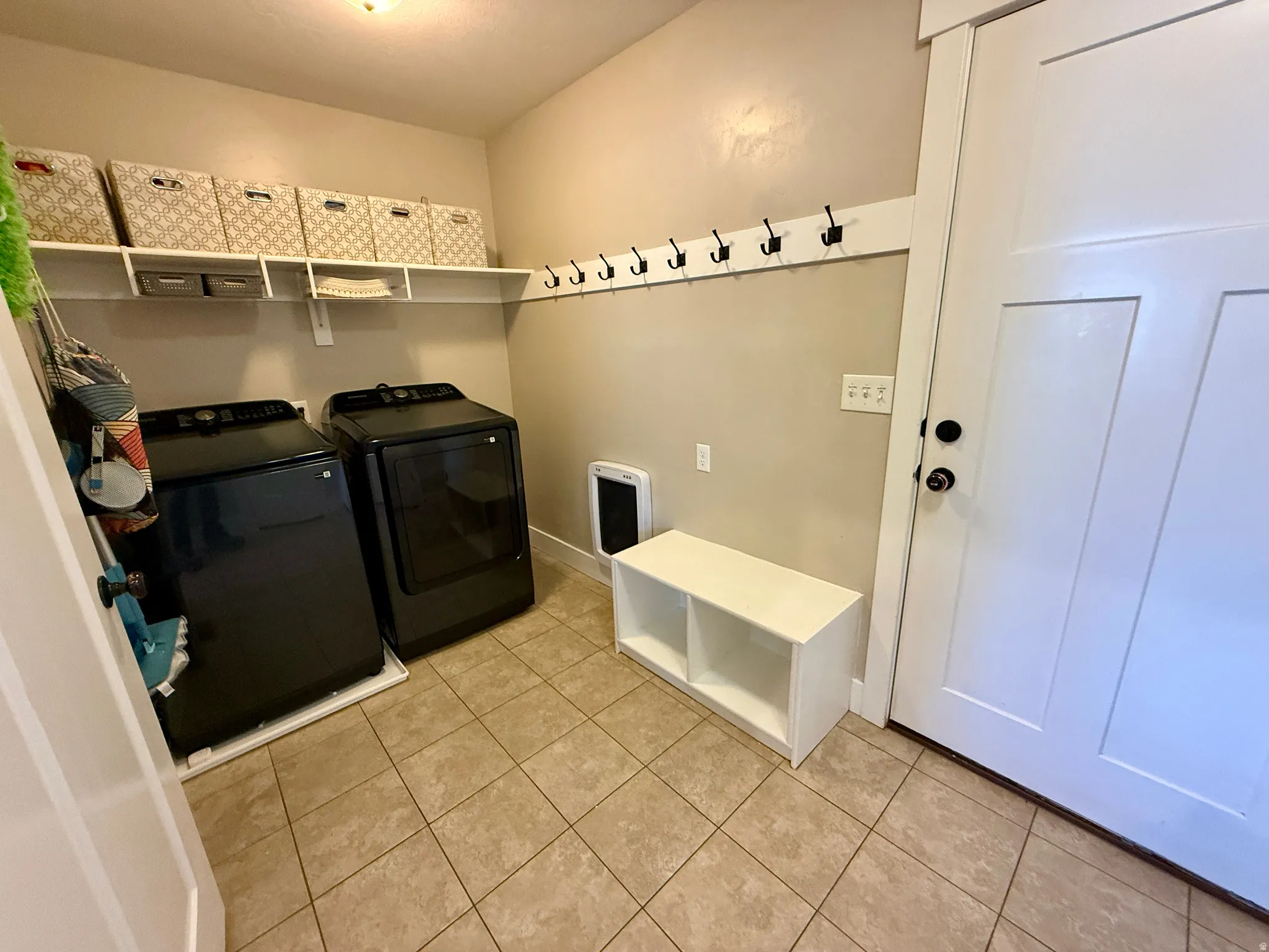Dedicated laundry room featuring tile flooring, built-in shelving, and wall-mounted coat hooks