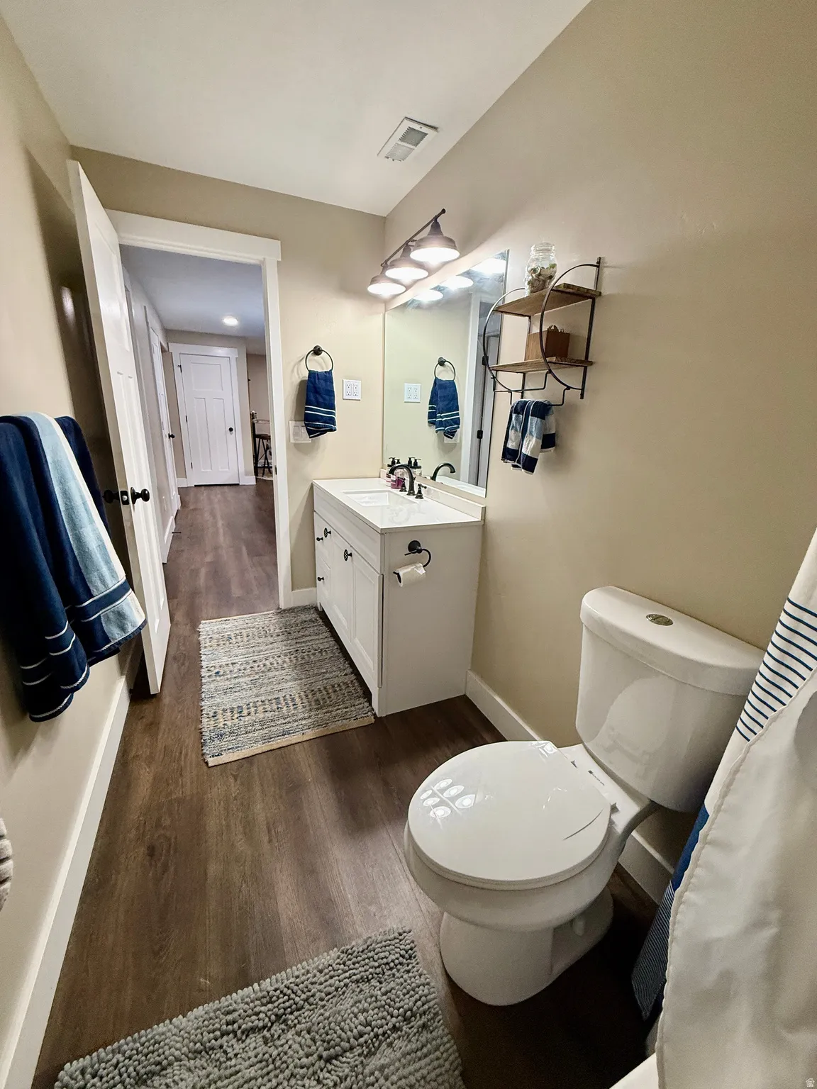 Full bathroom featuring a white vanity with integrated sink, dark wood-finish flooring, and contemporary light fixture