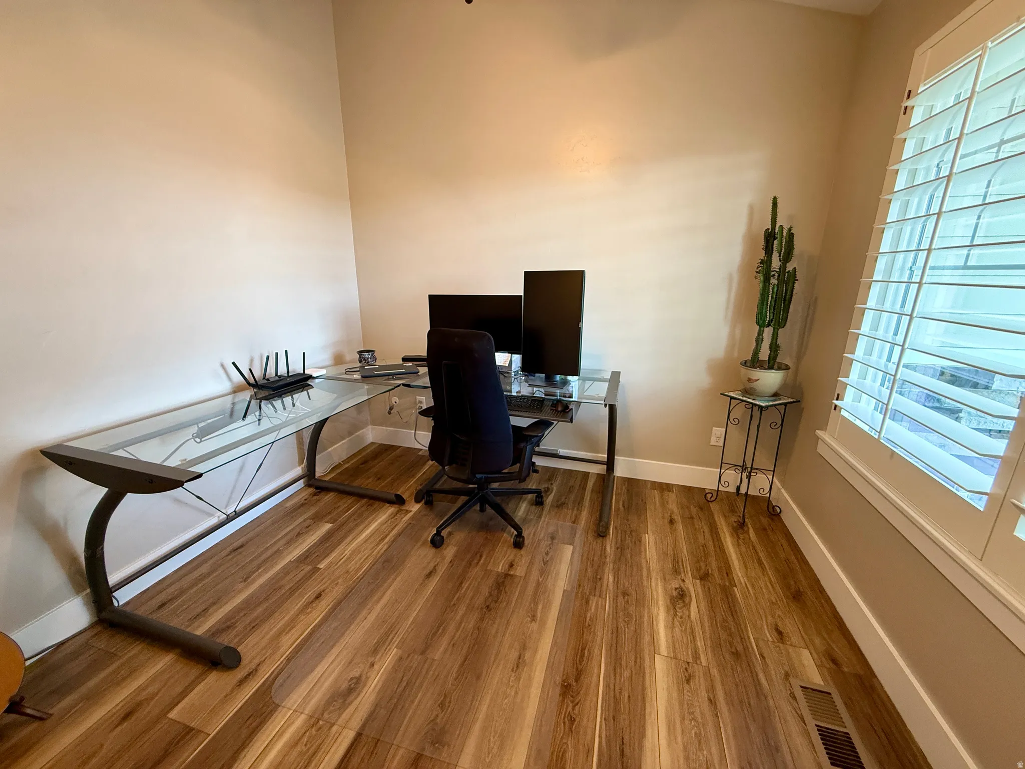 Room with wood-finish flooring, neutral wall tones, and plantation shutters