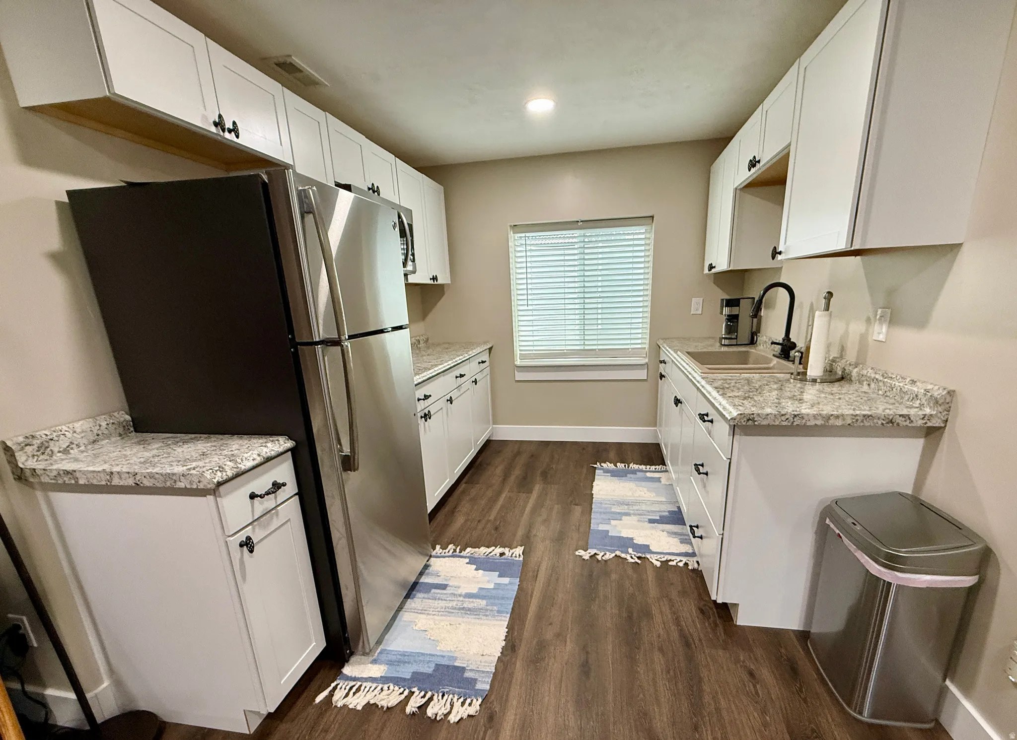 U-shaped kitchen featuring white cabinetry, light-toned countertops, stainless steel appliances, a double basin sink with a matte black faucet, and wood-finish flooring