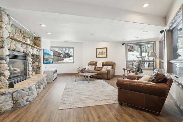 Spacious living area featuring a floor-to-ceiling stone fireplace with a raised hearth, wood-finish flooring, recessed lighting, and large windows