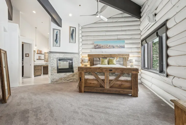 Spacious bedroom featuring log-style wall finishes, a stone-clad fireplace with a built-in firebox, and high vaulted ceilings with exposed beams