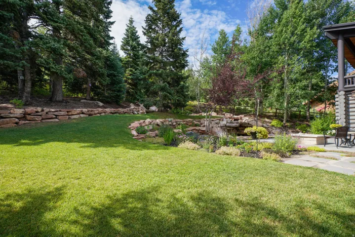 Expansive lawn bordered by a stone retaining wall and mature evergreen trees