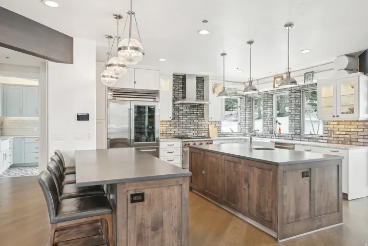 Gourmet kitchen featuring a large central island with integrated sink, wood-finish flooring, white cabinetry, professional-grade stainless steel appliances, and a stacked brick backsplash