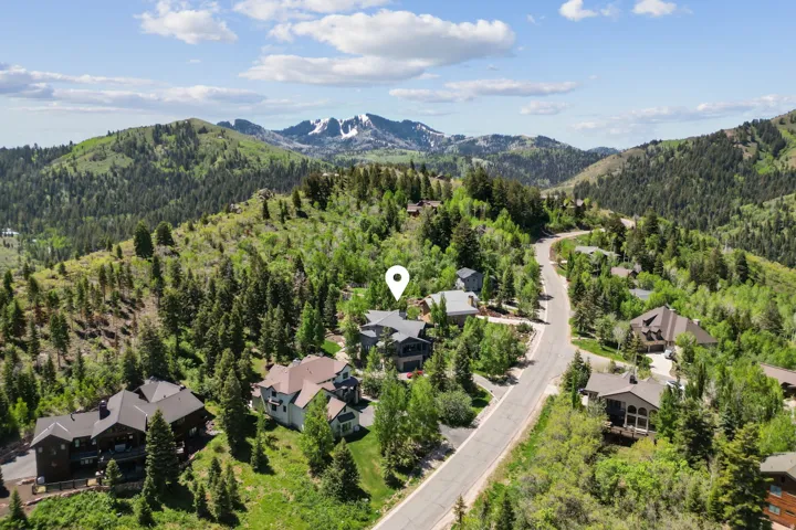 Mountainous terrain featuring a paved road, scattered residences, and extensive tree coverage under a partly cloudy sky