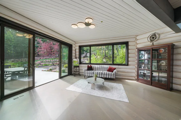 Spacious interior featuring a large sliding glass door, a picture window, wood-finish flooring, log-style walls, and a planked ceiling with a contemporary light fixture