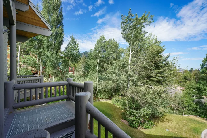 Private outdoor deck featuring log railing, open-grate flooring, wood-paneled eaves, and a backdrop of mature trees