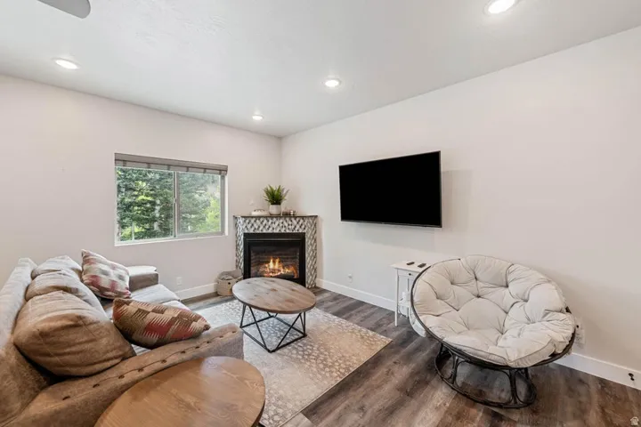 Living area featuring a corner fireplace with mosaic tile surround, a window offering exterior views, recessed lighting, and wood-finish flooring