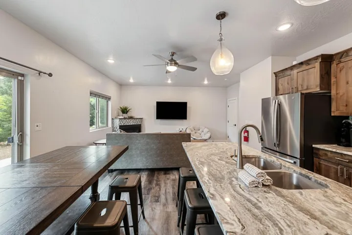 Kitchen island featuring a double basin stainless steel sink with a gooseneck faucet, light-toned stone countertop, and pendant lighting
