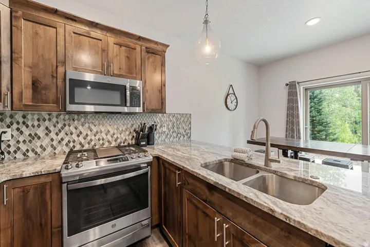 Kitchen featuring wood cabinetry, stainless steel appliances, granite countertops, a mosaic tile backsplash, and a double basin sink with a gooseneck faucet