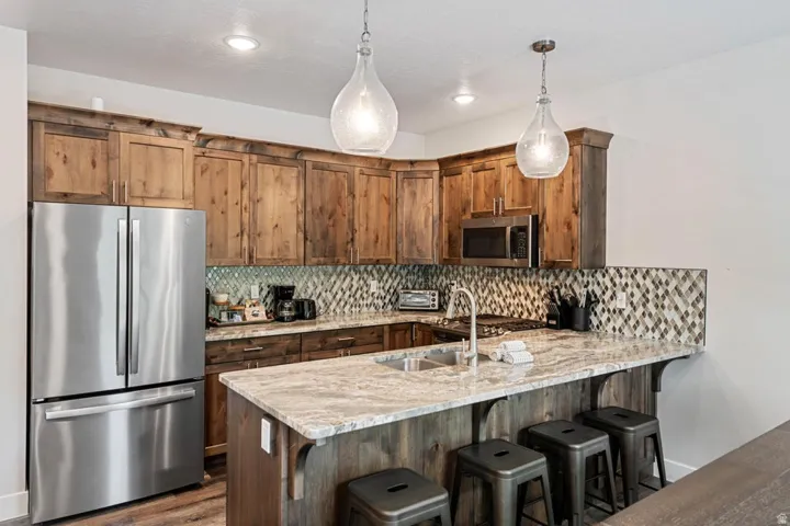 Kitchen featuring wood-finish cabinetry, stainless steel appliances, a multi-tone mosaic tile backsplash, and a large island with integrated sink