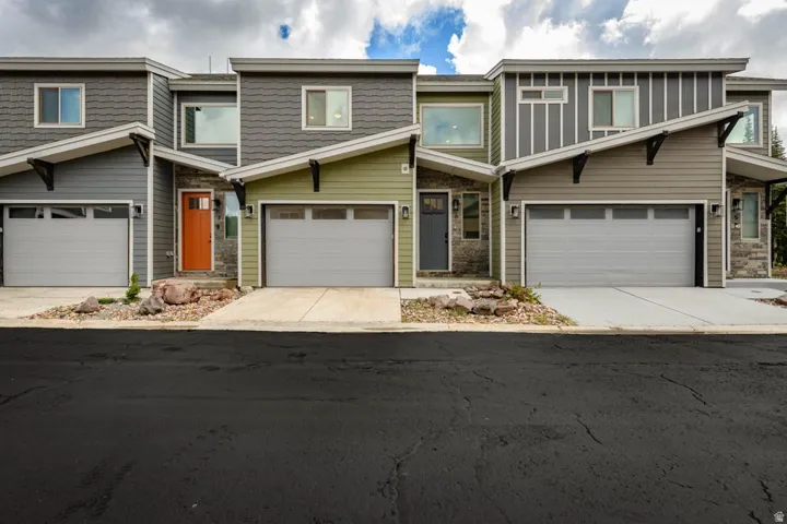 Modern multi-unit building with varied exterior siding, stone accents, individual garages, and contrasting entry doors