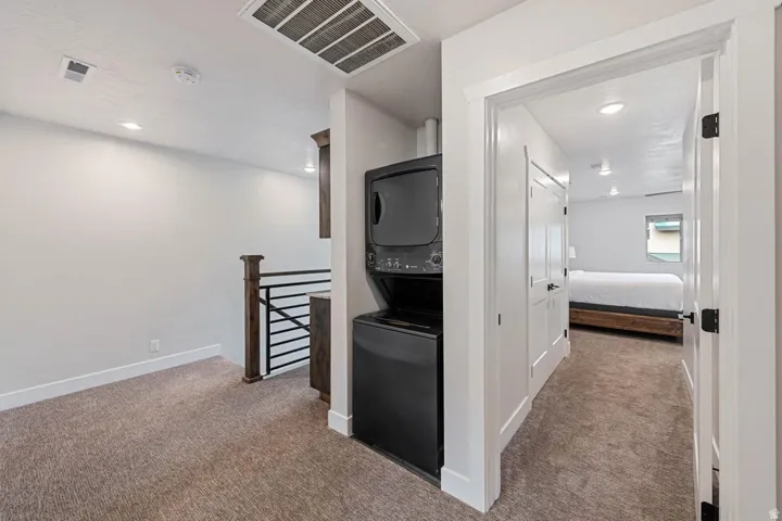 Upper-level hallway featuring a stacked black washer and dryer, recessed lighting, and neutral carpeting