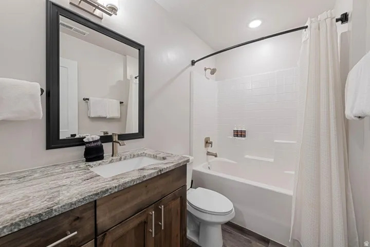 Bathroom featuring a wood-finish vanity with a stone countertop, an undermount sink, a framed mirror, and a full bathtub with a shower