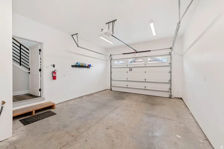 Attached garage featuring a white overhead door with top-panel windows, concrete flooring, and an interior access door with modern black railing