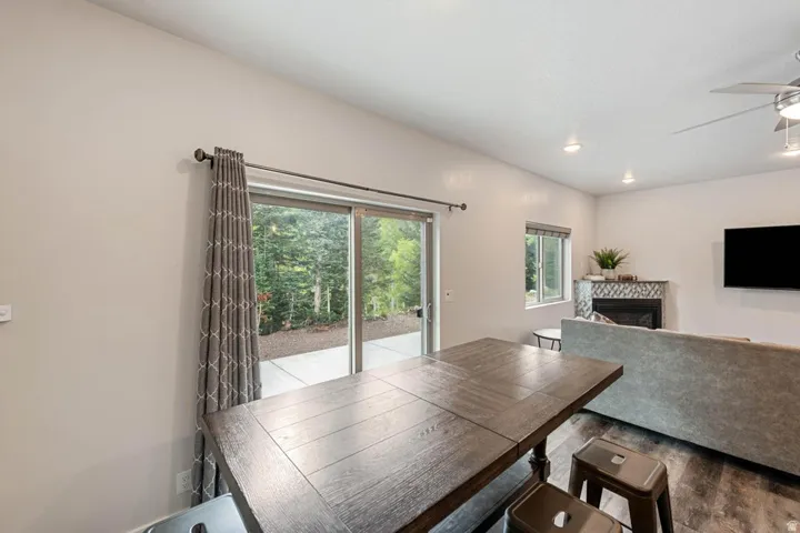 Dining area featuring a dark wood-finish table with two stools, a sliding glass door providing outdoor access, and a window with blinds