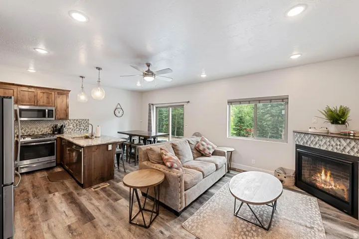 Open-concept living area featuring wood-finish flooring, a kitchen island with stone countertop, stainless steel appliances, a tiled fireplace, and recessed lighting