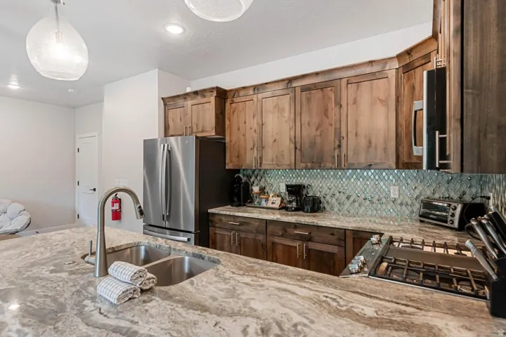 Kitchen featuring a gas cooktop, stainless steel appliances, a double basin sink with a high-arch faucet, wood cabinetry, and a tile backsplash