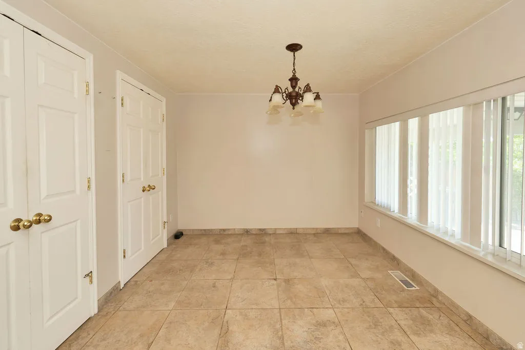 Spacious room featuring tile flooring, a multi-panel window with vertical blinds, and a traditional chandelier