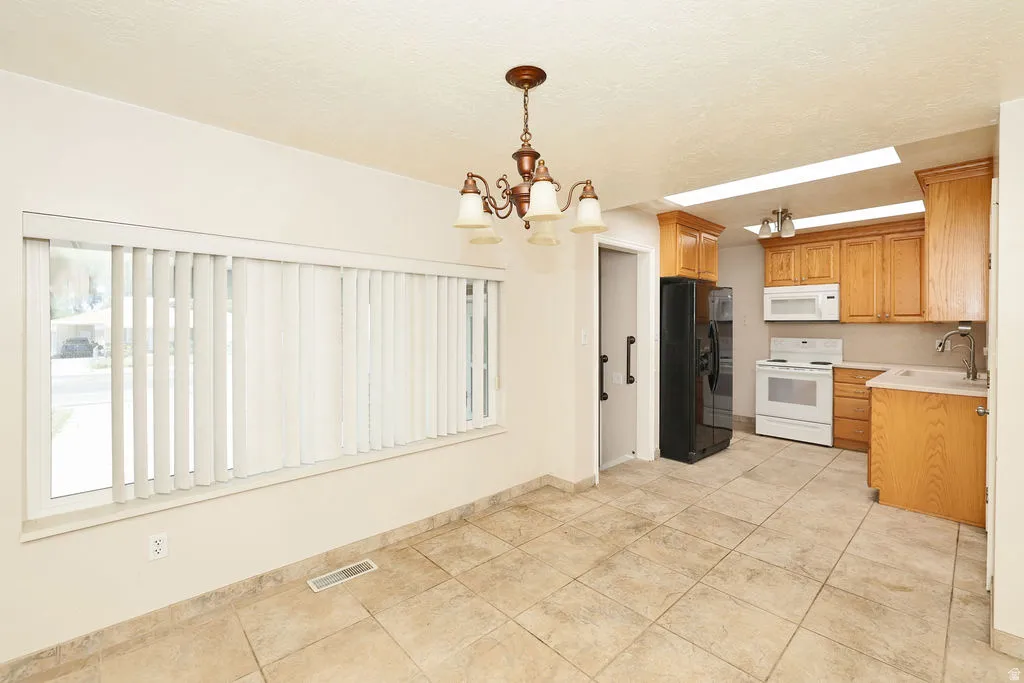 Kitchen and dining area featuring tile flooring, a window with vertical blinds, a bronze chandelier, wood cabinetry, and white appliances