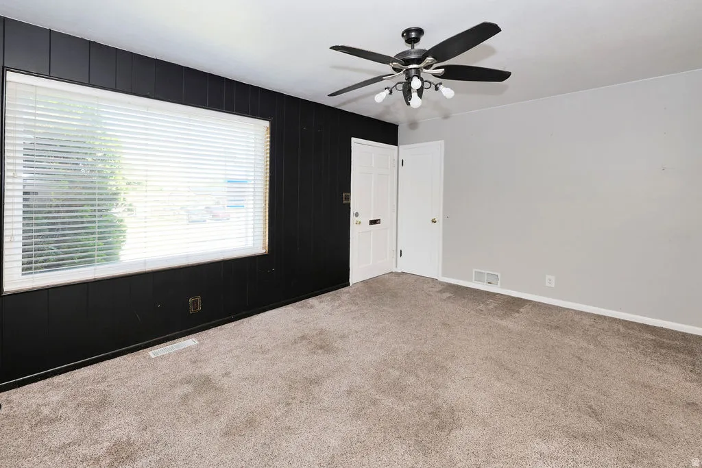 Carpeted interior space featuring a large window with horizontal blinds, a ceiling fan with integrated lighting, and a white paneled door