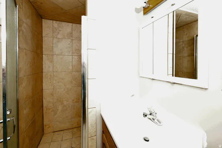 Tiled shower enclosure with a clear glass door, complemented by a white vanity with an integrated sink and a mirrored medicine cabinet