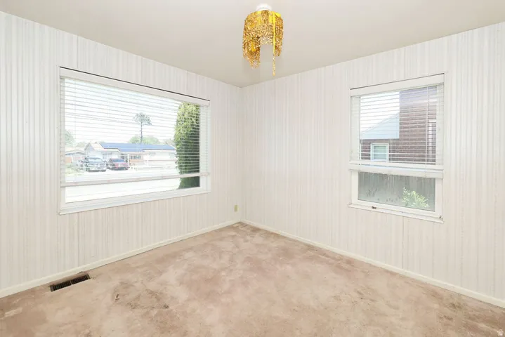 Room featuring two windows with horizontal blinds, textured wall coverings, and carpeted flooring
