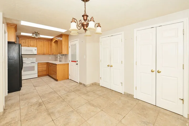 Kitchen and dining area featuring light-toned wood cabinetry, a built-in microwave, white electric range, black refrigerator, and tile flooring
