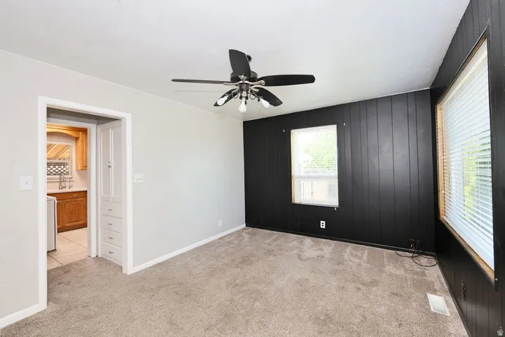Carpeted room featuring a ceiling fan, a black accent wall with vertical paneling, and two windows with blinds