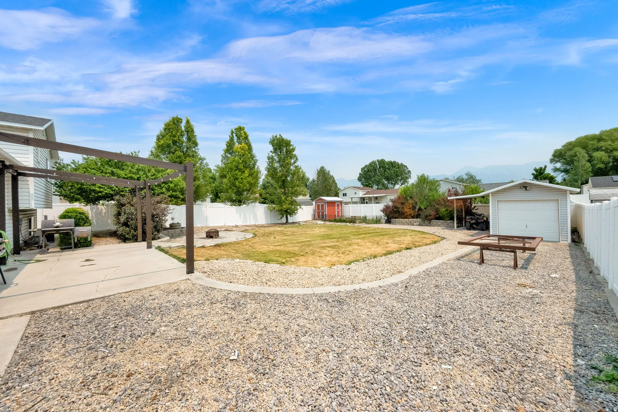 Expansive backyard featuring a concrete patio with a pergola, gravel RV parking, a central lawn area, and a detached garage with workshop.