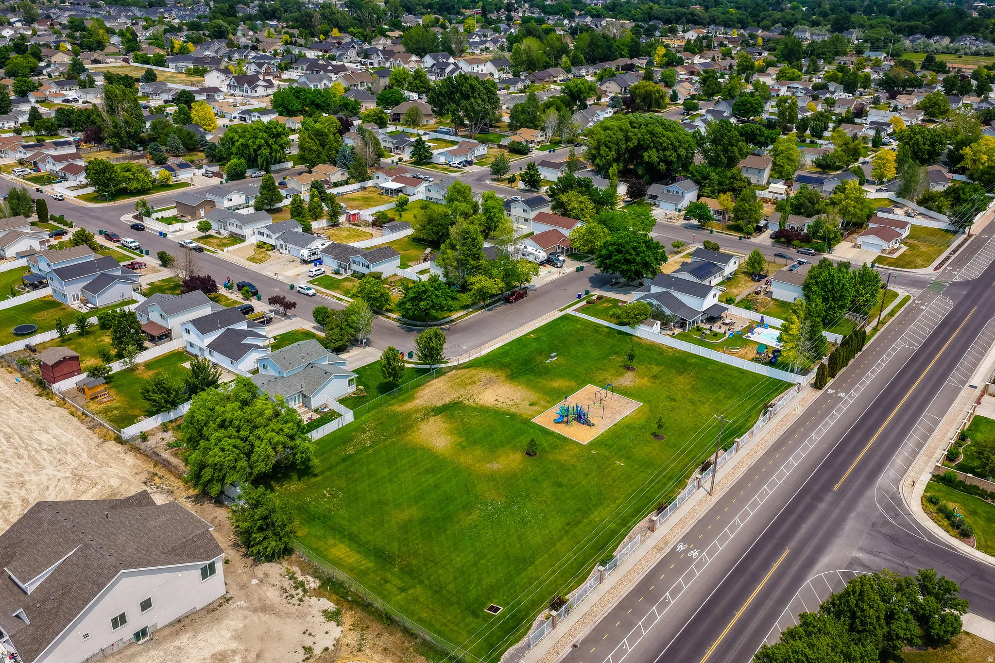 Aerial perspective showcasing a residential area with diverse home styles, mature trees, and a community green space featuring recreational equipment