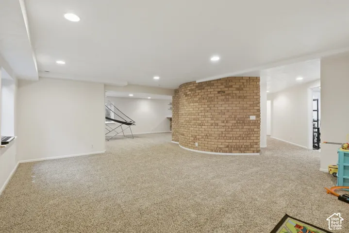 Spacious carpeted room featuring recessed lighting, light-toned walls, and a curved brick accent wall