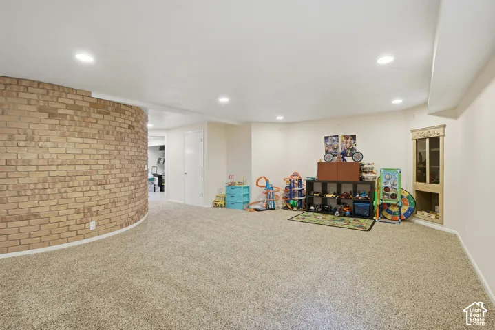 Spacious lower level featuring recessed lighting, light-toned carpeting, a curved brick accent wall, and an integrated corner display cabinet