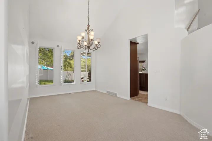 Vaulted ceiling room featuring a decorative chandelier, three windows with white plantation shutters, and light-toned carpeting
