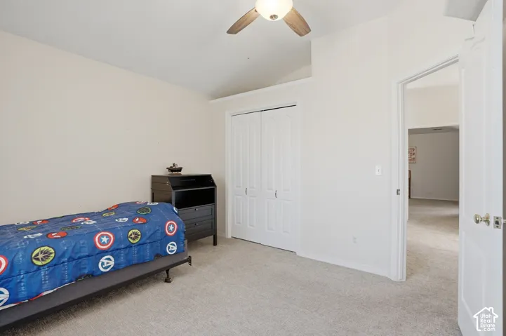 Carpeted interior room featuring a bi-fold closet door, vaulted ceiling, and ceiling fan with integrated lighting